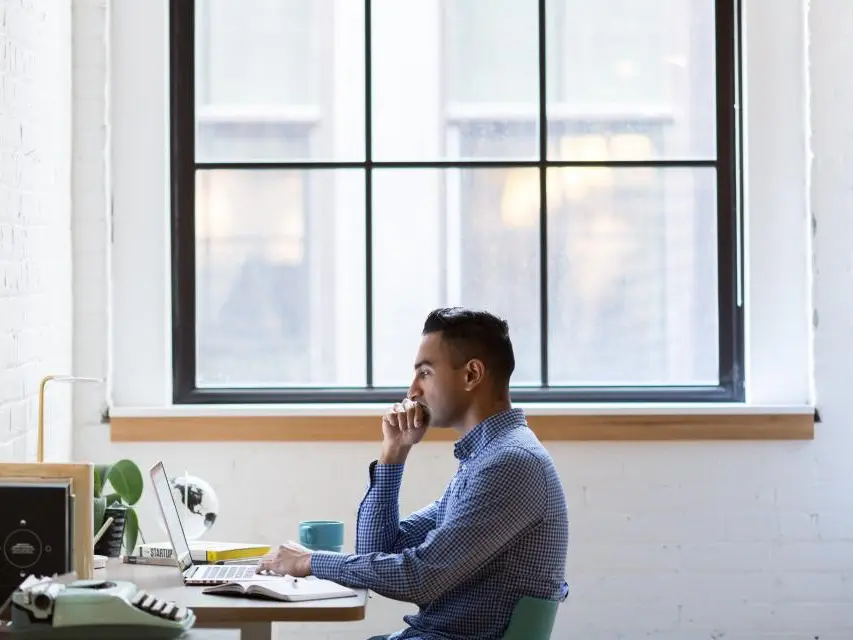 A man at a desk by a tall window, thinking something over